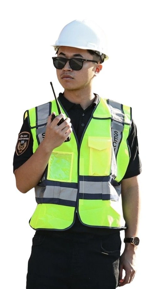 construction security guard standing with radio in his hand, reflective vest on, and construction hard hat